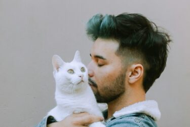 Man met zwart haar knuffelt zijn witte kat en de kat vindt dat fijn